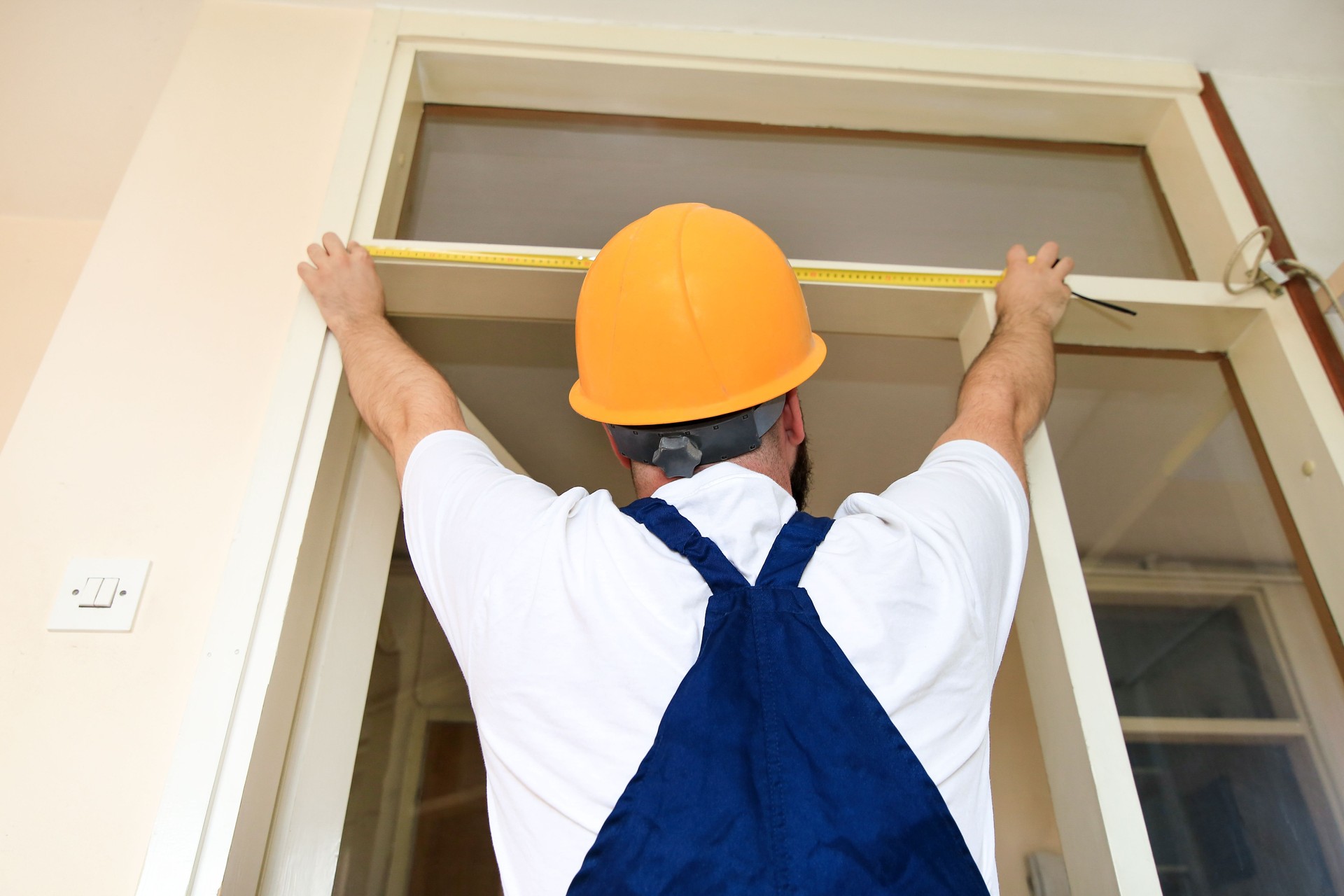 Operaio edile e tuttofare sta lavorando alla ristrutturazione dell'appartamento. Il costruttore sta misurando la porta della stanza usando il metro in cantiere. Concetto di ristrutturazione. Strumenti di costruzione e assistenza.